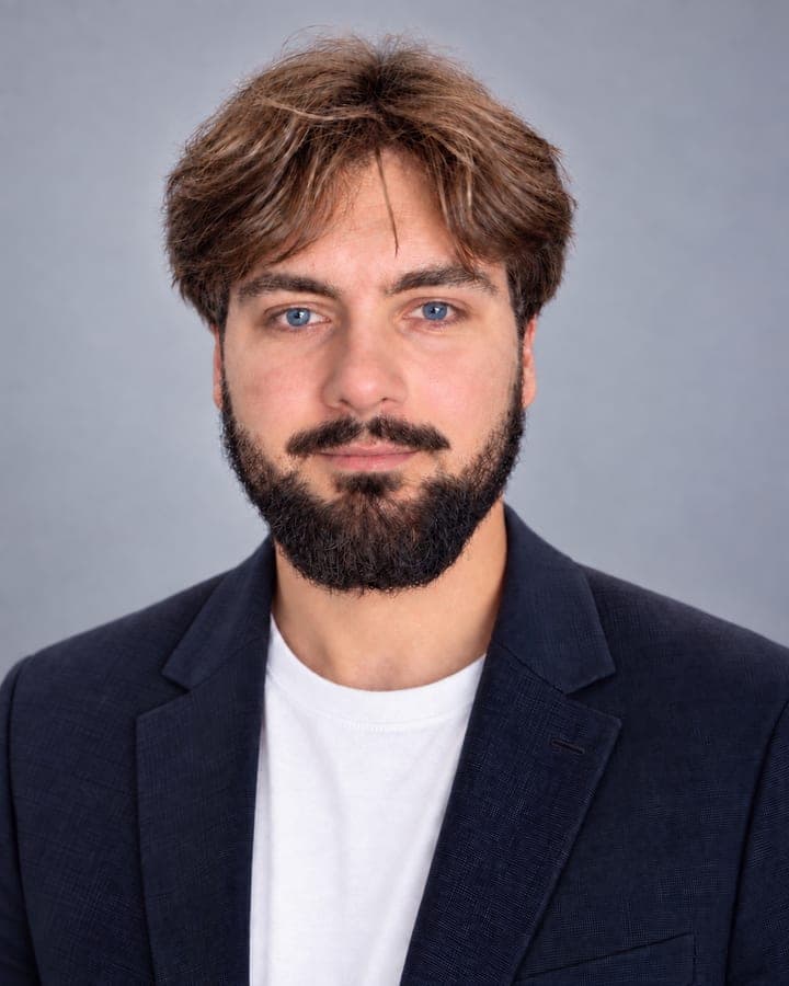 Portrait d'Andréas Chatti, en veste bleu marine et t-shirt blanc sur fond gris.